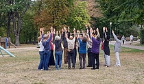 Gruppenbild mit Menschen die die Arme zum Himmel heben im Park.