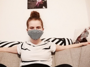 Junge Frau mit Maske auf einem Sofa.